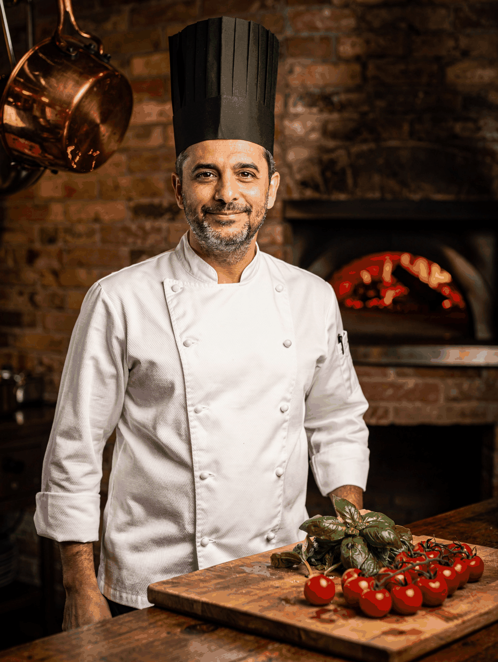 Sous Chef Matteo inspecting wood-fired dishes over open hearth embers